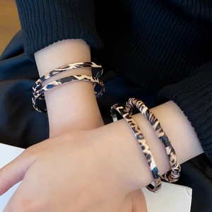 Detail view of a slim leopard print twisted cuff bracelet worn on a female wrist