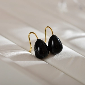 Detail view of water drop earrings featuring polished black stone and gold hook