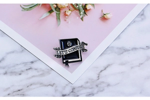 Macro shot of a black and white book enamel pin with a pentagram and Let's Conjure text