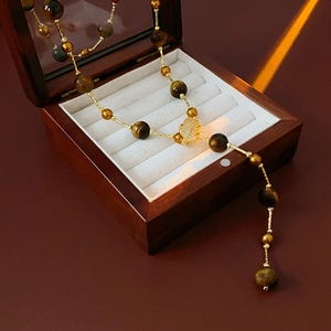 Detailed view of long tiger eye stone necklace with gold leaf pendant in a wooden jewelry box