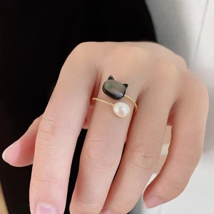 Close-up of golden open ring with cat-shaped shell charm and white pearl on finger