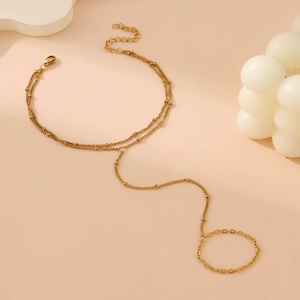 Elegant gold double-layer hand chain bracelet with small beads and ring on orange background