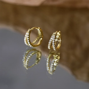 Macro shot of gold double-row pavé hoop earrings with zircon stones on a mirror surface