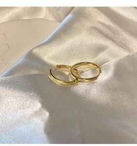 Close-up of gold minimalist hoop earrings resting on white silk fabric background