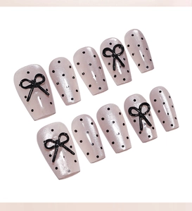 Detail of pink pearlescent press-on nails with black polka dots and 3D ribbon bows