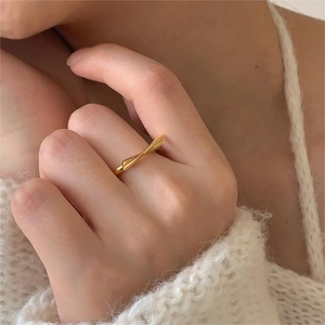 Detail of a slender gold bow knot ring worn on finger with a minimalist twisted design