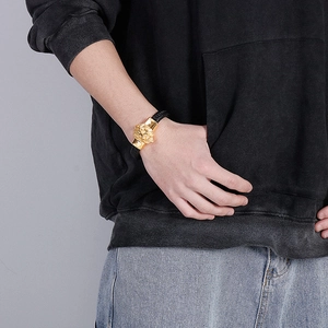 Detail of men's braided leather bracelet featuring a gold lion head charm on a model's wrist
