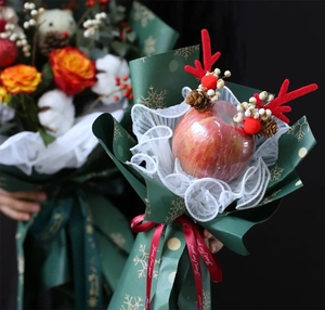 Close-up of Christmas gift apple with red reindeer antlers, berries and pine cones