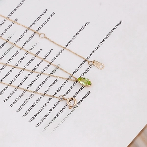 Macro detail of G9K gold chain with olive green marquise-cut gemstone on white paper