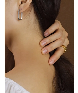 Dettaglio di orecchini a U argentati e anello a treccia dorato indossati da una modella