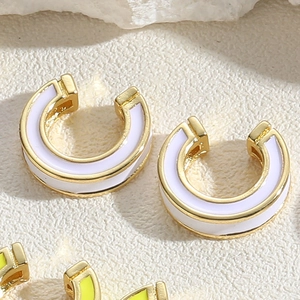 Detailed macro view of gold C-shape enamel earrings on a textured stone surface