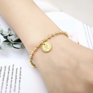 Detail of 18K gold bead bracelet with Queen Elizabeth II coin charm worn on wrist