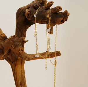 Detailed close-up of gold chain necklace with round crystal zircon tassels on driftwood
