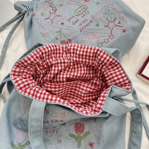 Detail of blue denim tote bag showing colorful embroidery and red plaid cotton lining