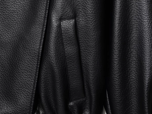 Detailaufnahme der schwarzen Lychee-Narben-Lederstruktur und Taschennähte an der Jacke
