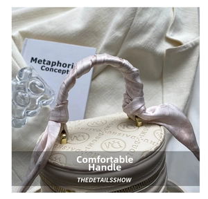Close-up of beige cylindrical bucket bag with silk scarf handle and gold zipper detail