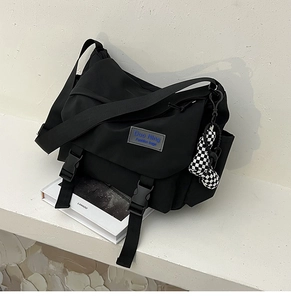 Detail of black nylon messenger bag with adjustable strap and checkered ball charm