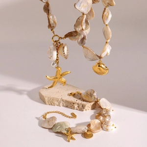 Close-up of golden necklace and bracelet with seashells and starfish on a stone