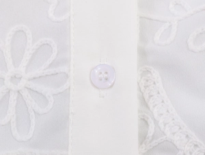 Close-up of intricate floral embroidery and white resin button on a white cotton shirt