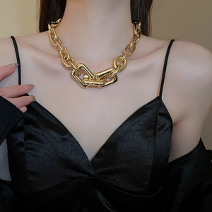 Close-up of a chunky gold-toned chain necklace with oversized geometric links on neck