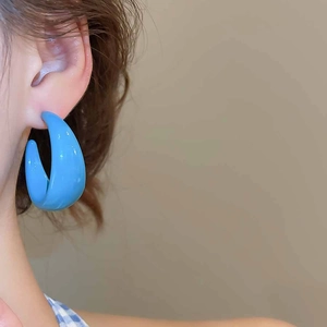 Close-up of a glossy bright blue acrylic C-shaped hoop earring worn on a model ear