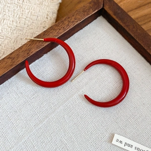 Close-up of red enamel C-shaped earrings with gold metal posts on a linen background