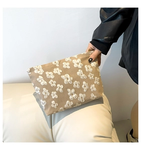 Detail of beige makeup bag with 3D white floral texture held against black leather jacket
