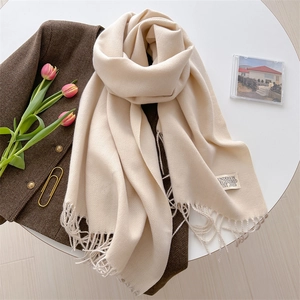 Detailed close-up of beige pashmina scarf with fringe edge and brand tag on a table