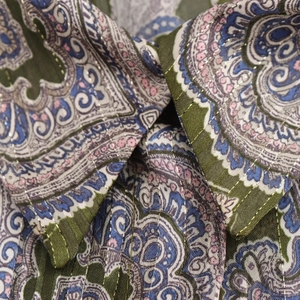 Detail of paisley print blouse with metallic gold stitching on green and blue fabric