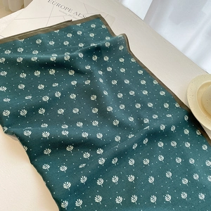 Detailed view of dark green printed silk scarf with white leaf pattern and stitched edges