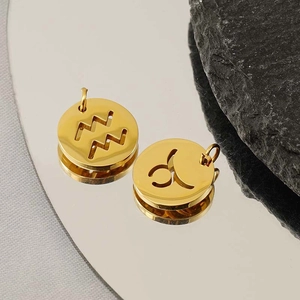 Golden zodiac pendants with Aquarius and Taurus hollowed symbols on a reflective surface