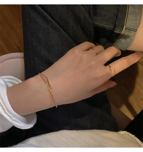 Detailed view of gold double-layer bracelet and minimalist cubic zirconia rings on hand