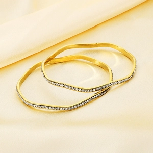 Detailed view of two gold wavy bangles with pave crystals on soft satin fabric