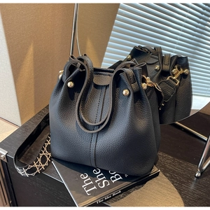 Detail of black leather bucket bag with gold hardware and woven strap against a mirror