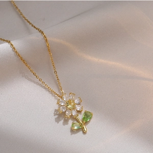 Elegant gold flower necklace with white petals and green leaves on soft fabric background