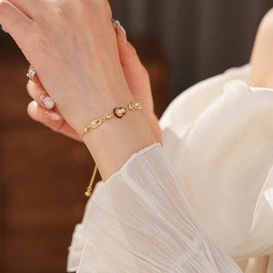 Macro detail of a gold-plated pearl bracelet with a red heart pendant on a model wrist