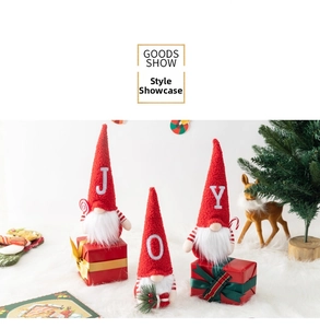 Three Christmas gnomes with JOY letters on red knitted hats atop festive gift boxes