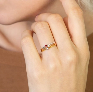 Detalle de tres anillos finos apilables con piedras de colores en un dedo de mujer.
