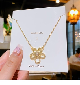 Detail of a gold flower pendant necklace with zircon inlay on a white display card