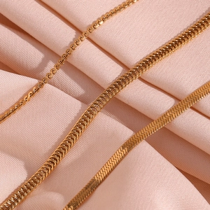 Detailed view of three 18K gold plated stainless steel box and rope chains on pink fabric