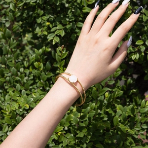 Close-up of golden twisted rope bangle featuring a polished white stone on green leaves