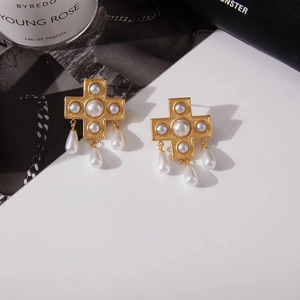 Dettaglio di orecchini a croce in oro vintage con perle rotonde e a goccia di imitazione
