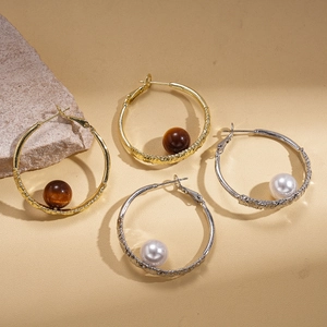 Textured gold and silver hoop earrings with faux pearl and resin beads on leather background