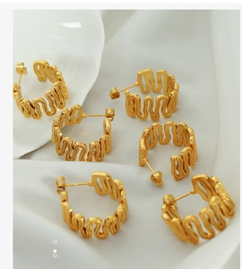 Close-up of golden C-shaped wave earrings with textured grain finish on a white tray
