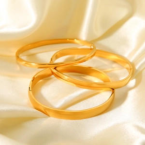 Macro shot of four polished gold-plated stainless steel bangles on beige satin fabric