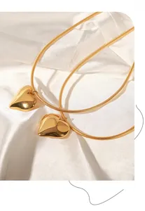 Detailed macro view of two golden hollow heart pendants on snake chains over white silk