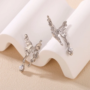 Silver liquid metal butterfly earrings with white pearl drops on a minimalist display