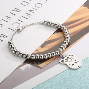 Close-up of a silver beaded chain bracelet featuring a cute hollow pig charm on a magazine