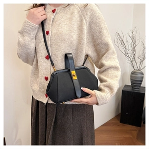Close-up of black shell handbag with gold hardware clasp on woman wearing heart sweater