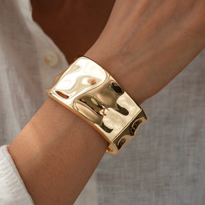 Minimalist wide gold bangle with irregular hammered texture and shiny metallic finish